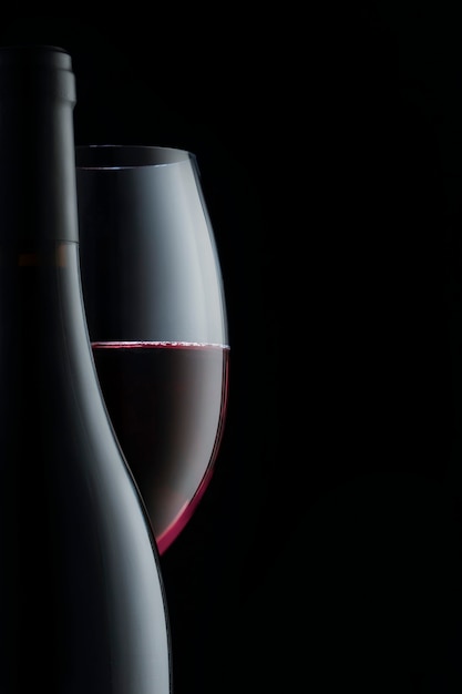 Bouteille élégante et verre de vin rouge isolé sur fond noir