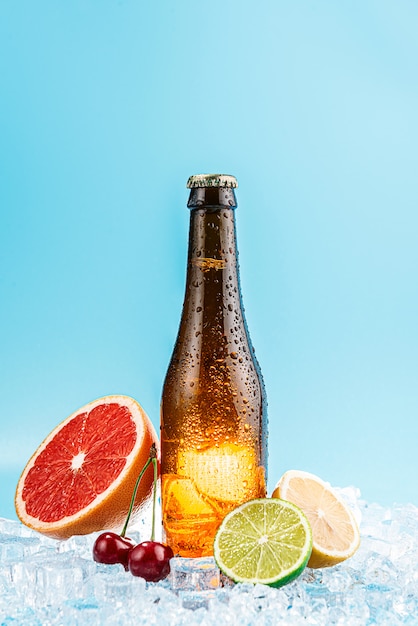 Bouteille fermée de bière en verre brun sur la glace. les fruits sont à proximité. concept de bière artisanale de fruits ou de cidre