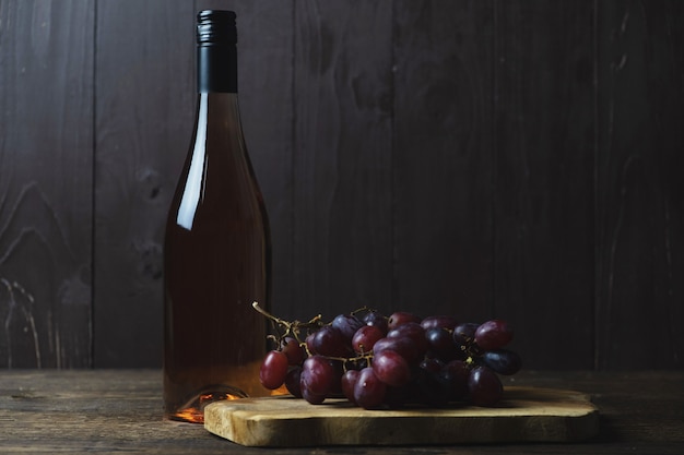 Une bouteille fermée de vin rosé et une grappe de raisins rouges sans pépins près de bois