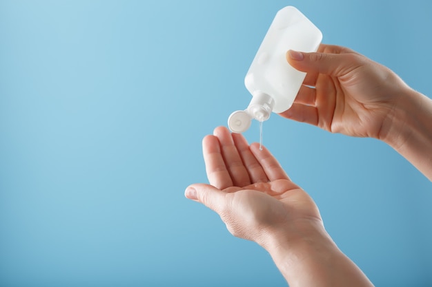 Une bouteille de gel désinfectant dans vos mains sur un fond bleu. Traitement antiseptique des mains contre les bactéries Sanitizer.