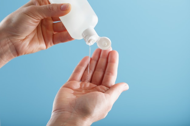 Une Bouteille De Gel Désinfectant Dans Vos Mains Sur Un Fond Bleu. Traitement Antiseptique Des Mains Contre Les Bactéries Sanitizer.