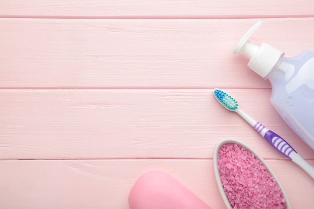 Bouteille de gel douche rose, savon, sel de bain et brosse à dents sur le mur rose. Vue de dessus