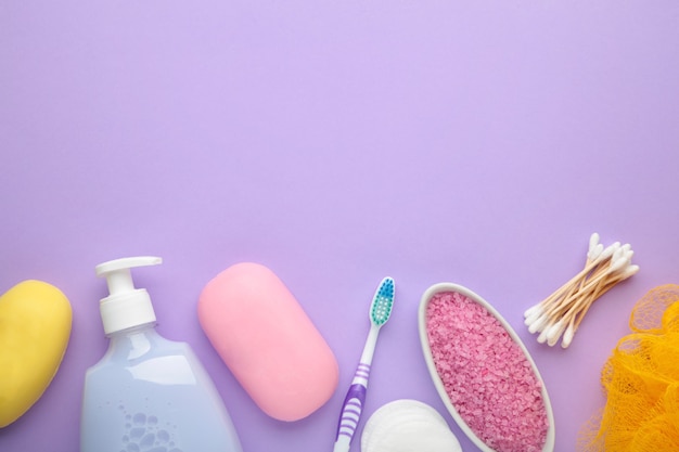 Bouteille de gel douche rose, savon, sel de bain et brosse à dents sur mur violet. Vue de dessus