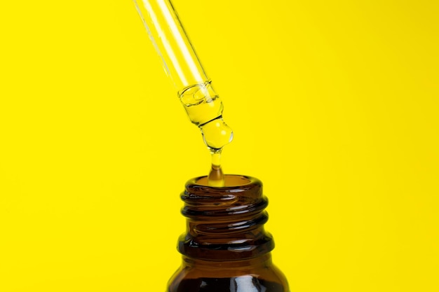 Photo bouteille d'huile cosmétique avec une pipette sur fond jaune gros plan goutte de liquide dégoulinant médecine de beauté et concept de soins de santé macro photo cosmétiques écologiques naturels