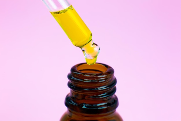 Bouteille d'huile cosmétique avec une pipette sur fond rose. Gros plan sur les gouttes de liquide. Concept de beauté, de médecine et de soins de santé. Macrophotographie. Cosmétiques naturels et écologiques.