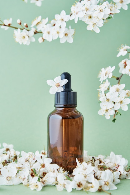 Bouteille d'huile essentielle avec branche de plante en fleurs sur fond vert