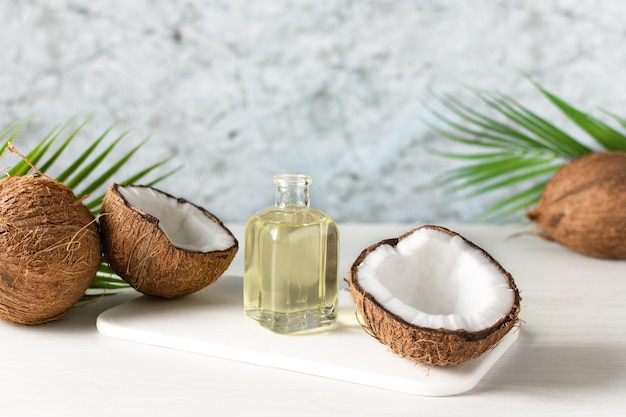 Photo bouteille d'huile de noix de coco et noix de coco fraîches avec feuille de palmier sur table en bois blanc