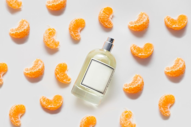 Une bouteille d'huile parfumée ou de parfum sur un mur blanc, décorée de tranches de mandarine. Le concept d'un parfum d'agrumes ou d'aromathérapie, des arômes fruités.