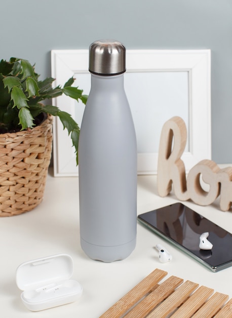 Bouteille isotherme gris sur un bureau blanc entouré de gadgets modernes et vue de face de l'usine