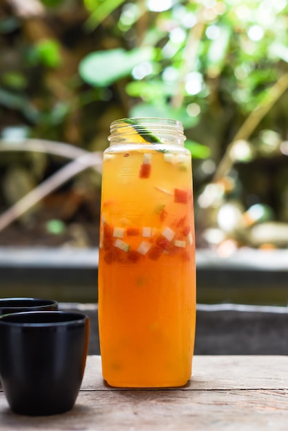 Bouteille de jus frais fait maison à base d'oranges, de pastèque, de citron vert sur la table en bois avec des tasses