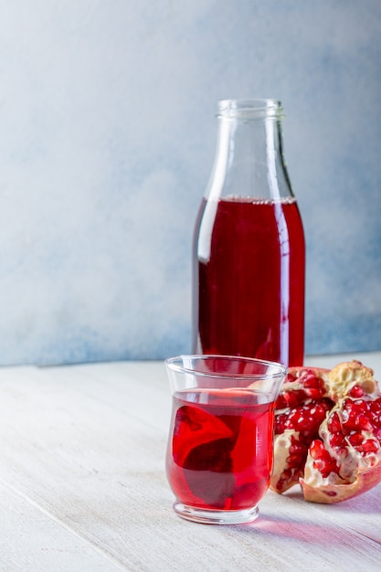 Bouteille de jus de grenade et un verre, grenade mûre, entière et pelée sur un fond en bois blanc