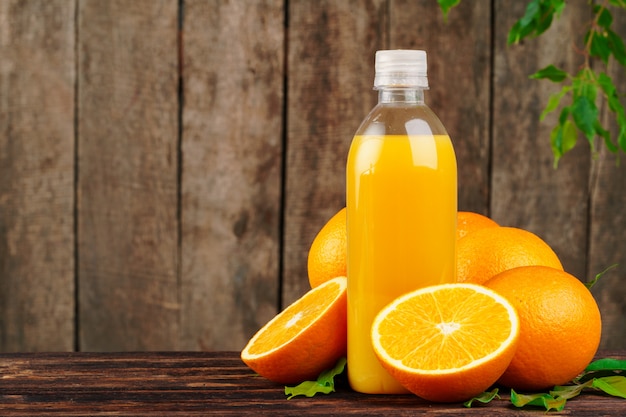 Bouteille de jus d'orange avec des oranges sur table en bois