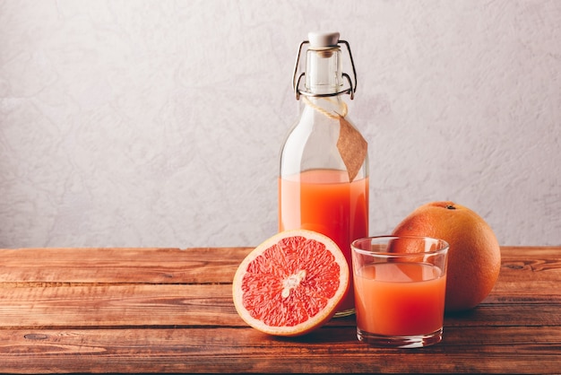 Bouteille de jus de pamplemousse avec verre et fruits sur une surface en bois