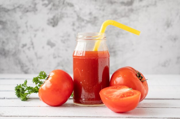 Bouteille de jus de tomate et tomates fraîches sur une table en bois.