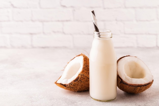 Une bouteille de lait de coco et de noix de coco sur fond clair.