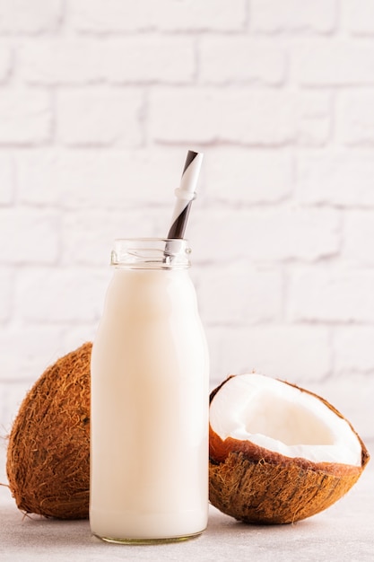 Une bouteille de lait de coco et de noix de coco sur fond clair.