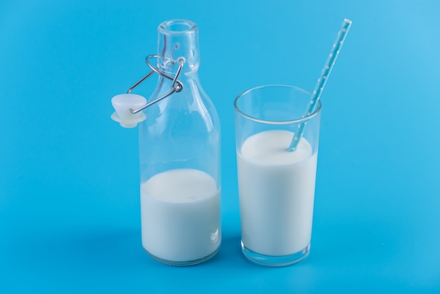Bouteille de lait frais et un verre avec une paille sur un fond bleu. Concept de produits laitiers sains contenant du calcium