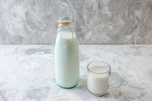 bouteille de lait vue de face et verre de lait sur fond gris