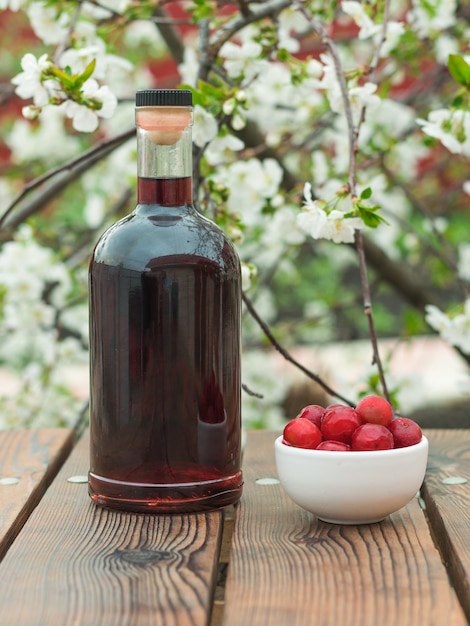 Une bouteille de liqueur de cerise et de baies de cerise congelées d'un arbre en fleurs. Alcool fait maison à base de baies de cerise.