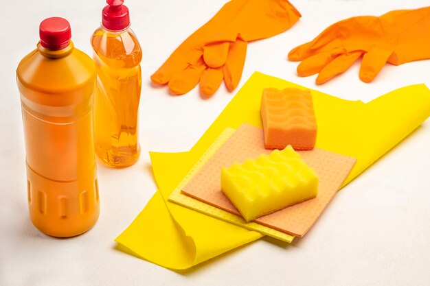 Bouteille de liquide orange, éponge jaune et chiffon jaune. Gants en caoutchouc orange. Produits chimiques ménagers pour nettoyer l'appartement. Fond blanc. Vue de dessus