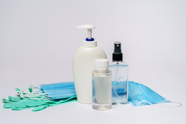 bouteille de lotion, de désinfectant ou de savon liquide, des gants en latex de caoutchouc et un masque de protection sur une table gris clair