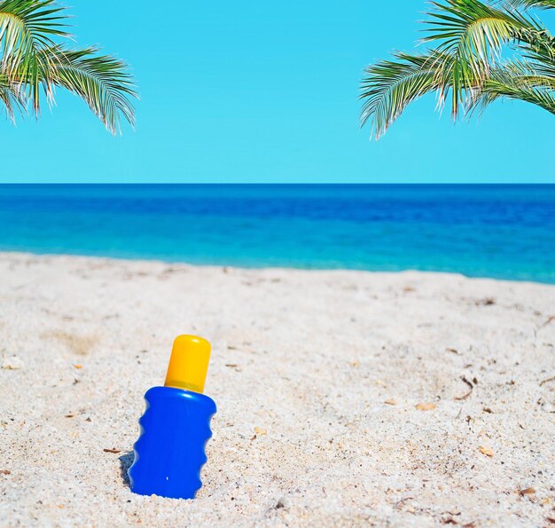 Bouteille de lotion solaire dans le sable avec des palmiers