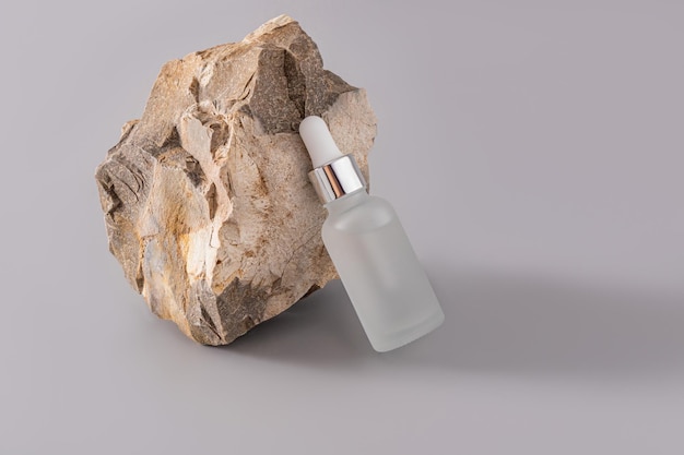 Une bouteille matte de soins de la peau organiques appuyée sur une grande pierre texturée Cosmétiques naturels fond gris