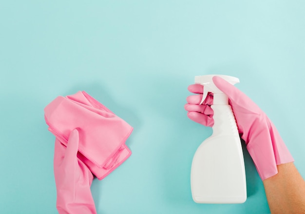 Bouteille de nettoyage et gant de toilette dans les mains avec des gants en caoutchouc rose Fond bleu