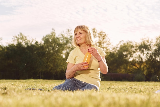 Bouteille orange dans les mains Femme âgée ayant un beau week-end à l'extérieur sur le terrain à la journée ensoleillée