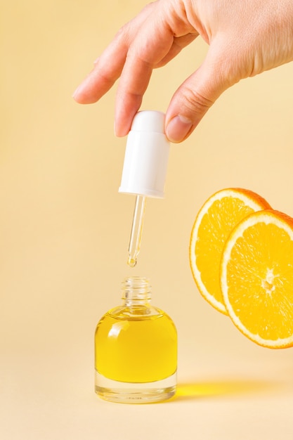 Bouteille orange ouverte avec pipette dans la main de la femme sur fond jaune clair