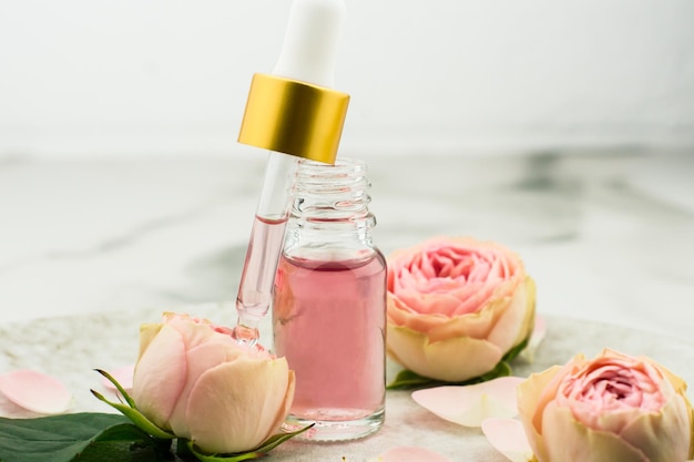 Une bouteille ouverte d'huile de rose et une pipette remplie de produits cosmétiques pour le rajeunissement et les soins de la peau du visage sur fond de marbre.