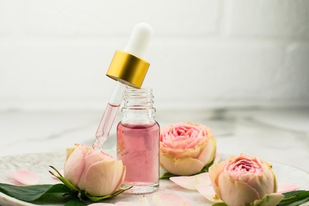 Une bouteille ouverte d'huile de rose et une pipette remplie de produits cosmétiques pour le rajeunissement et les soins de la peau du visage sur une plaque en céramique.