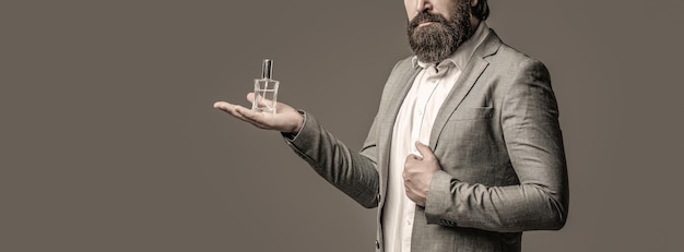 Bouteille de parfum ou d'eau de Cologne, parfumerie, cosmétiques, bouteille d'eau de Cologne parfumée, homme tenant l'eau de Cologne. Parfumerie masculine, homme barbu en costume. Homme tenant une bouteille de parfum.