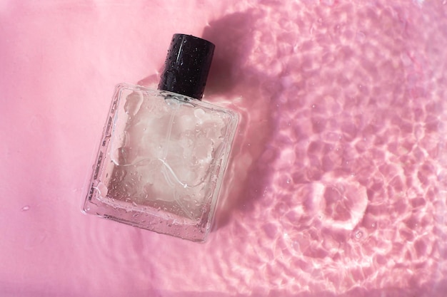 Bouteille de parfum sur le fond et gouttes d'eau Une bouteille de parfum sans inscriptions Odeur Parfum sur fond rose Gouttes d'eau Espace de copie