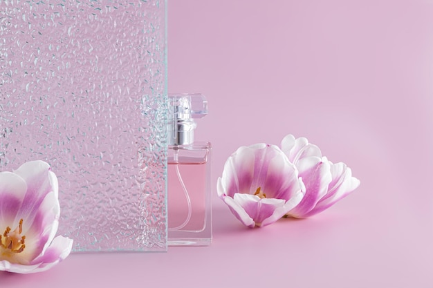 Une bouteille de parfum pour femme ou d'eau de toilette se tient derrière un verre en relief sur fond violet avec une présentation d'arôme de fleurs printanières fraîches