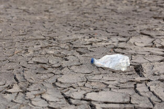 Bouteille en plastique froissée vide sur le désert sec de boue fissurée comme fond gris