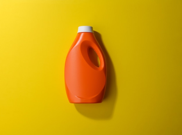 Bouteille en plastique orange pour lessive liquide sur surface jaune, vue de dessus