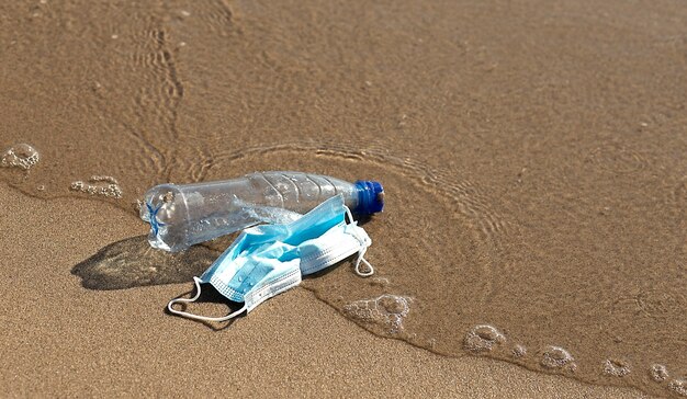 une bouteille en plastique se trouve et un masque médical sur la plage et pollue la mer.