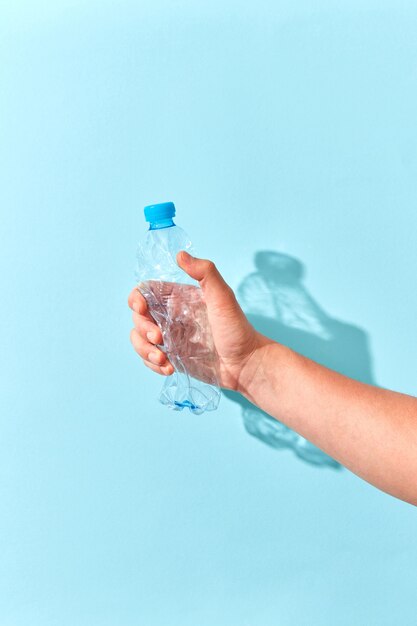 Bouteille en plastique vide écrasée à la main sur un mur bleu pastel avec des ombres transparentes. Place pour le texte. Problème écologique de la pollution de l'environnement.