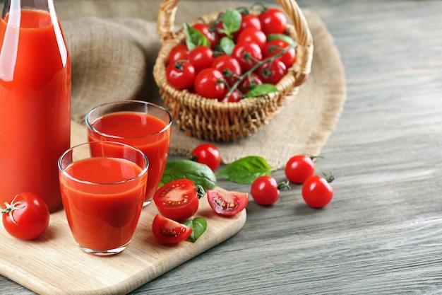 Bouteille pleine et verres de jus de tomate avec des légumes sur une table en bois se bouchent