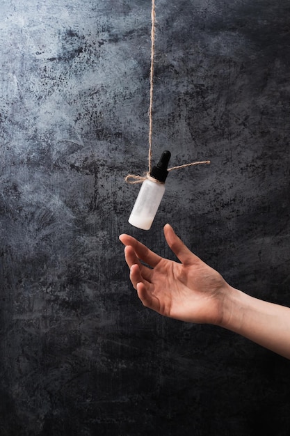 Bouteille de produit cosmétique à côté de mains humaines sur fond sombre Affiche photo verticale