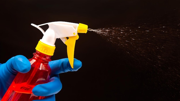 Bouteille de pulvérisateur d'eau dans une main avec des gants sur fond sombre avec des articles ménagers à vaporiser liquide pour la maison