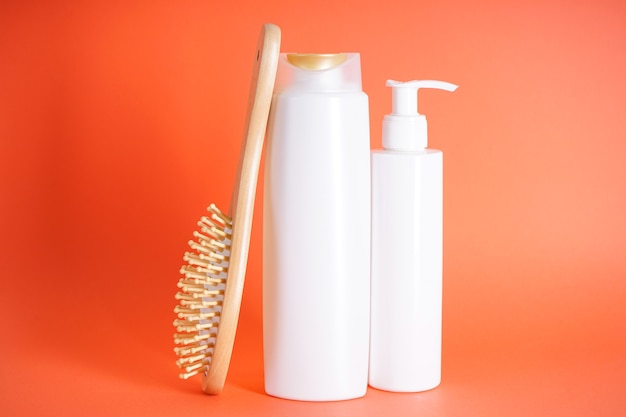 Bouteille de shampoing, distributeur de savon, brosse à cheveux en bois sur fond orange.