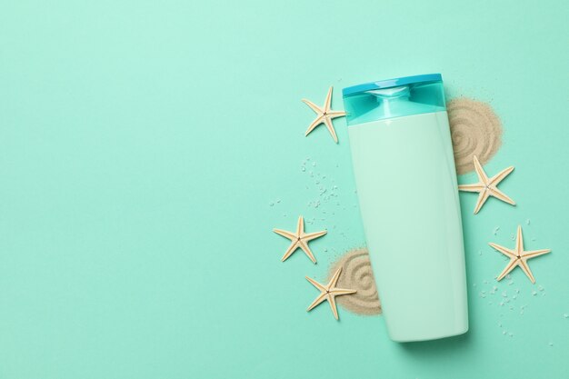 Bouteille de shampoing, étoiles de mer et sable sur fond de menthe