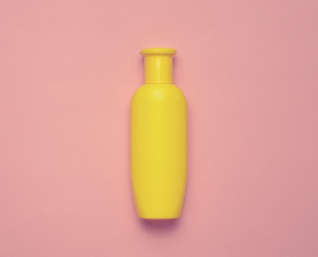 Bouteille de shampoing jaune sur fond rose pastel