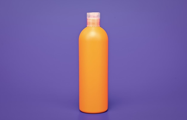Bouteille de shampoing orange sur fond bleu cosmétologie