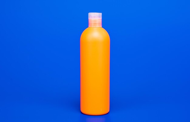 Bouteille de shampoing orange sur fond bleu, cosmétologie.