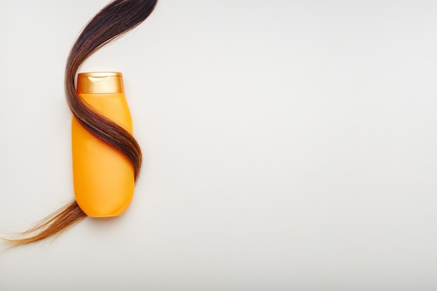 Bouteille de shampooing enveloppé dans une mèche de cheveux bouclés sur fond blanc avec copie espace. Produits cosmétiques pour le soin des cheveux, produits de beauté pour le traitement des cheveux.