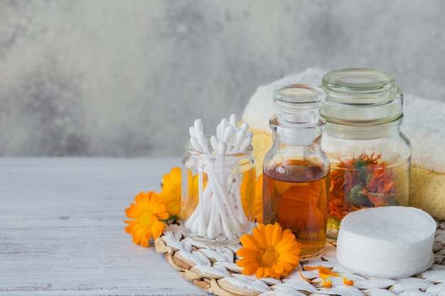 Une bouteille de teinture de souci ou d'infusion avec des fleurs de calendula fraîches et un coton et des bâtons sur blanc