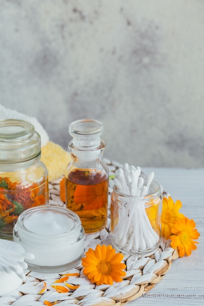 Une Bouteille De Teinture De Souci Ou D'infusion, De Pommade, De Crème Ou De Baume Avec Des Fleurs De Calendula Fraîches Et Sèches Et Un Coton Et Des Bâtons Sur Un Fond Blanc. Herbes Médicinales Naturelles.